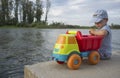 Little boy playing at riverside with dump truck loaded with stones Royalty Free Stock Photo