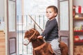 Two-year-old boy riding a rocking horse and holding a wooden sword