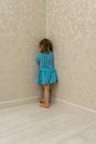 Two-year-old girl in blue dress stands punished in corner Royalty Free Stock Photo