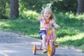 Two year-old laughing girl wearing corduroy flat cap and polka-dotted costume cycling kids pink and yellow tricycle Royalty Free Stock Photo