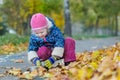 Two years old girl holding thermos flask cup hunkering at autumn foliage covering backdrop