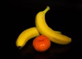 two yellow bananas and one orange tangerine Royalty Free Stock Photo