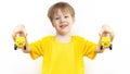 Two yellow cars with painted eyes and smile in hands of Little European happy happy child boy. Kid holds toy cars. Concept of