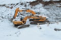 Two yellow crawler excavators dig ground in the pit in winter