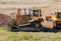 Two yellow dozers on a dirt terrain with blue sky