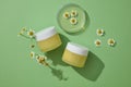 Two yellow jars container cream or mask decorated with chamomilla flowers on the green background Royalty Free Stock Photo