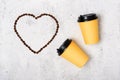 Two yellow paper cups lie to the right on a light gray concrete background. Copyspace in the shape of a heart made from coffee