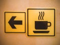 Two yellow square signs depicting arrow and cup hang on the wall. Photo with filter