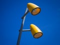 Two yellow street lamps with blue sky