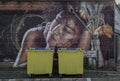 Two yellow Wheelie bin front of Portrait graffiti spray paint art