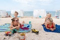 Two young adult caucasian female friends with cute little children enjoy having fun relaxing and sunbathing at sand sea Royalty Free Stock Photo