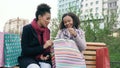 Two young african american women sharing their new purchases in shoppping bags with each other. Attractive girls talking