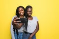 Two smiling young african girls taking a selfie isolated over yellow background Royalty Free Stock Photo