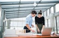 Two young architects with blueprints and model of a house standing in office, talking. Royalty Free Stock Photo