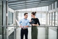 Two young architects with blueprints standing in office, talking. Royalty Free Stock Photo