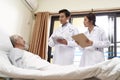 Two young asian doctors talking old man at bedside