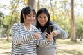 Two young Asian female best friends looking at a smartphone screen together while standing in a park Royalty Free Stock Photo