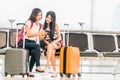 Two young Asian girl using smartphone check flight or web check-in, sit at airport waiting seat together