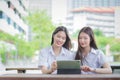 Two young Asian girls students are consulting together and using a tablet to search information for a study report while sitting Royalty Free Stock Photo