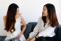 Two young Asian girls wearing office business style clothes sitting together on sofa, talking funny stories, smiling and laughing Royalty Free Stock Photo