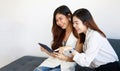 Two young Asian girls wearing office business style clothes sitting together on sofa using tablet computer serve internet with Royalty Free Stock Photo