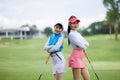 Two young asian women professional golfers stand and pose looking at camera and smiling taking photo at the golf course