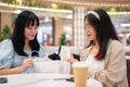 Two young Asian women sit in a cafe at a shopping mall, examining clothes they\'ve purchased Royalty Free Stock Photo