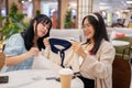 Two young Asian women sit in a cafe at a shopping mall, examining clothes they\'ve purchased Royalty Free Stock Photo