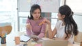 Two asian women sitting at office desk and talking about project startup ideas. Royalty Free Stock Photo