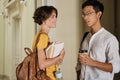 Two young attractive international students happily talking in corridor of university