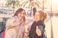 Two young attractive smiling women making thumb up gesture and holding coffee to go in their hands Royalty Free Stock Photo