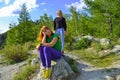 Two young beautiful blonde girls and redhead on a rock on a sunny warm autumnal summer day resting while traveling near a green t Royalty Free Stock Photo