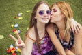 Two young beautiful blonde hipster girls on summer day having fun in european city. Green grass on a background and flower leafs. Royalty Free Stock Photo