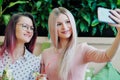 Two young beautiful girls, a blonde in a pink dress and a brunette with dyed hair, sit at a cafe table, drink lemonade Royalty Free Stock Photo