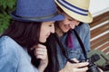 Two young beautiful girls in jeans dresses and hats sit on a bench in the park on a background of green plant walls, and Royalty Free Stock Photo