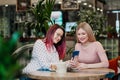 Two young beautiful girls sit in a green cafe at a table. Drink tea with croissants, chatting, laughing and taking Royalty Free Stock Photo