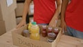 Two young and beautiful volunteers, man and woman, working together, putting products in a package for donations at a charity Royalty Free Stock Photo