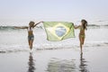 Two young beautiful women in bikini on beach running with Brazil flag