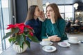 Two young beautiful women secretly sitting at a table in a coffee shop, girls whisper a secret in their ear Royalty Free Stock Photo