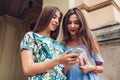 Two young beautiful women using smartphone outdoors. Girls checking social network on city street. Best friends