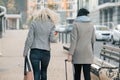 Two young beautiful women in warm clothes walking down the city street with a travel suitcase, women laughing and talking, view Royalty Free Stock Photo