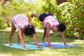 Two young Black friends in matching outfits do downward dog in park, fitness