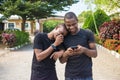 two young black men walking and holding each other laughing together while viewing content on a mobile phone. gay couple laughing Royalty Free Stock Photo