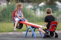 Two young blond children preschooler girl with long ponytail and cute school boy swing on see- saw on bright green blurred backgro Royalty Free Stock Photo