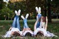 Two young blond women and one brunette girl, wearing white t-shirts, lying with their legs up on blanket on green grass in park, Royalty Free Stock Photo