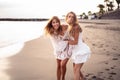 Two young blonde caucasian women walking on the beach, playing and laughing. Female friends having fun on the sea shore. Real Royalty Free Stock Photo