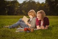 Two young boy studying lesson sitting on green grass in park. Brothers reading book together. Older brother helps younger making Royalty Free Stock Photo