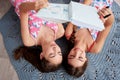 Two young brunette girls, wearing pink cotton pajamas, lying on grey carpet in light apartment, holding notebook, studying,