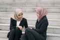 Two young business hijab woman, sitting on stairs and discussing while holding mobile phone Royalty Free Stock Photo