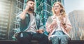 Two young business people are sitting on street. Hipster guy is talking on cell phone, girl is drinking coffee Royalty Free Stock Photo